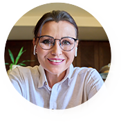 Smiling woman with glasses sitting indoors, wearing a light shirt.