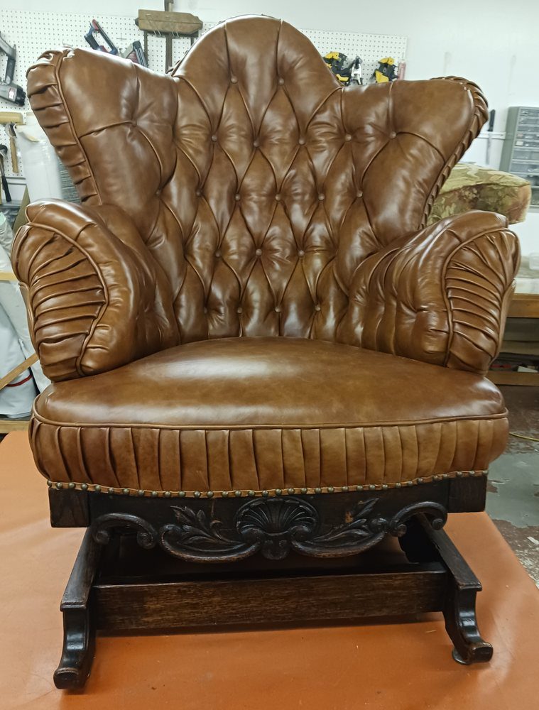 Vintage brown leather armchair with tufted back and carved wooden base.