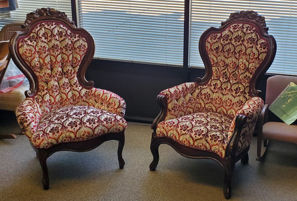 Two ornate vintage armchairs with patterned upholstery in a sunlit room.