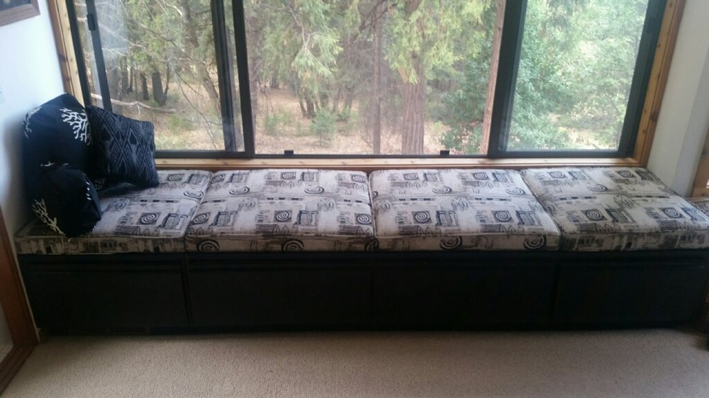 A cushioned window bench with patterned pillows and a view of trees outside.