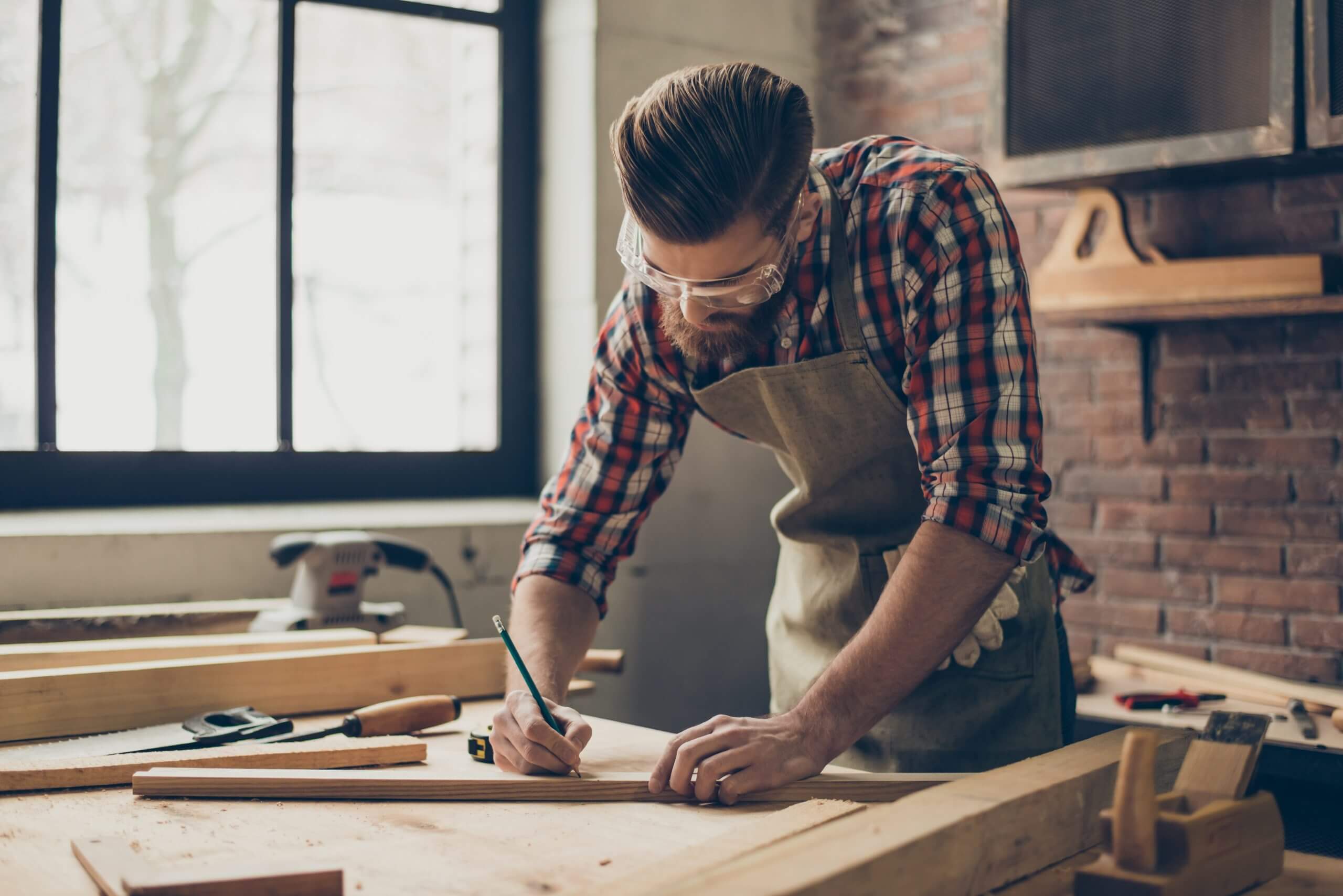 A man in an apron working on woodworking at a table.