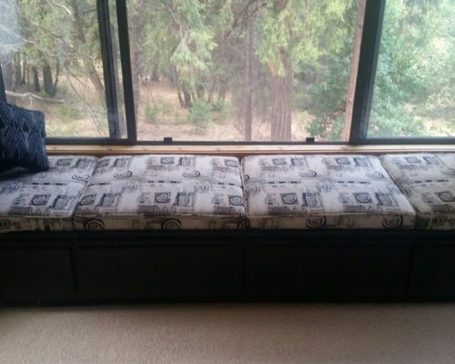 A cushioned window bench with patterned pillows and a view of trees outside.